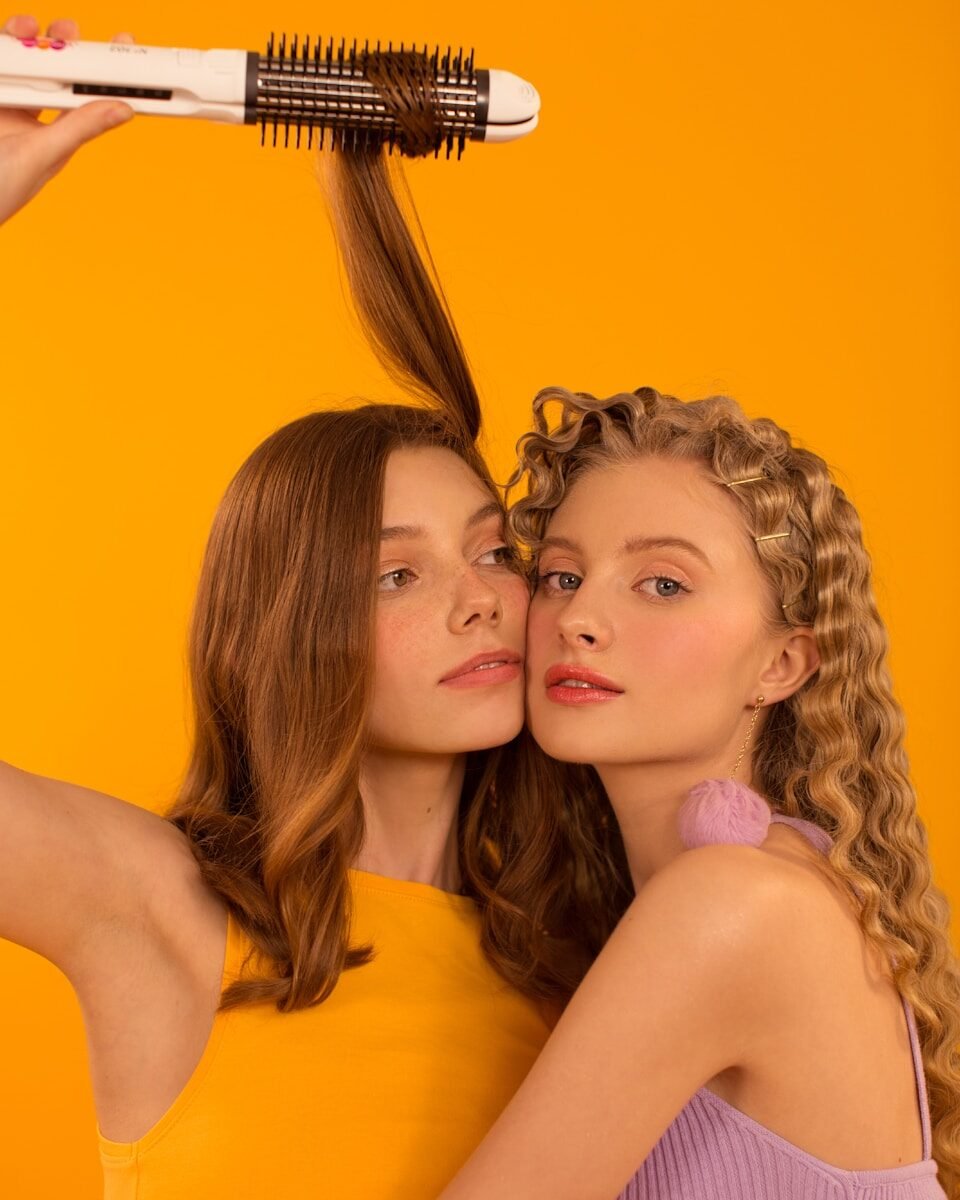 Two young women with different hairstyles and a hair tool