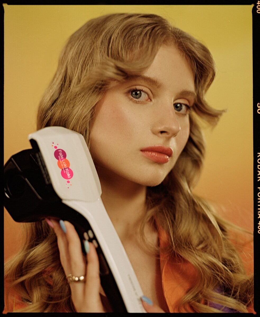 Young woman with wavy hair holds a white curling iron