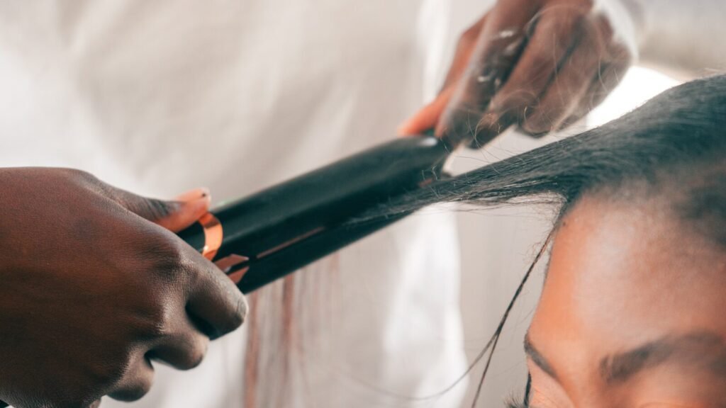 Hands straightening dark hair with a flat iron